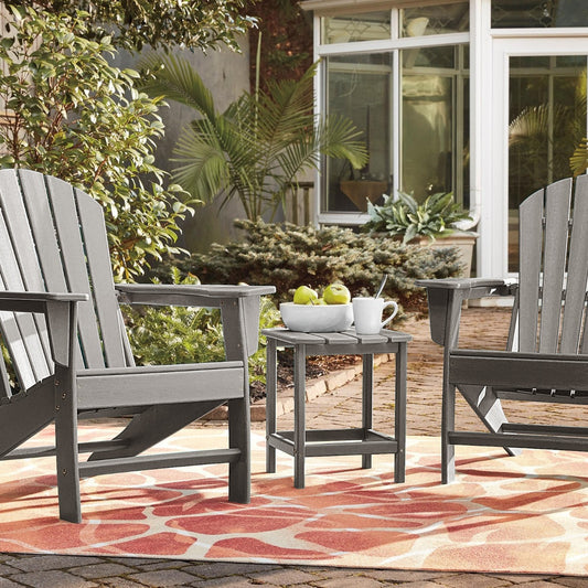 The patio table placed between two grey chairs on a patterned rug in a garden setting
