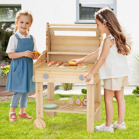 Two young girls playing with the wooden play kitchen set outdoors on a green lawn