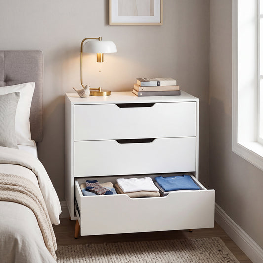 The white storage unit beside a bed with the bottom drawer open and filled with folded clothes