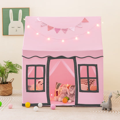 The pink play tent standing on a rug with star lights and bunting draped across the front