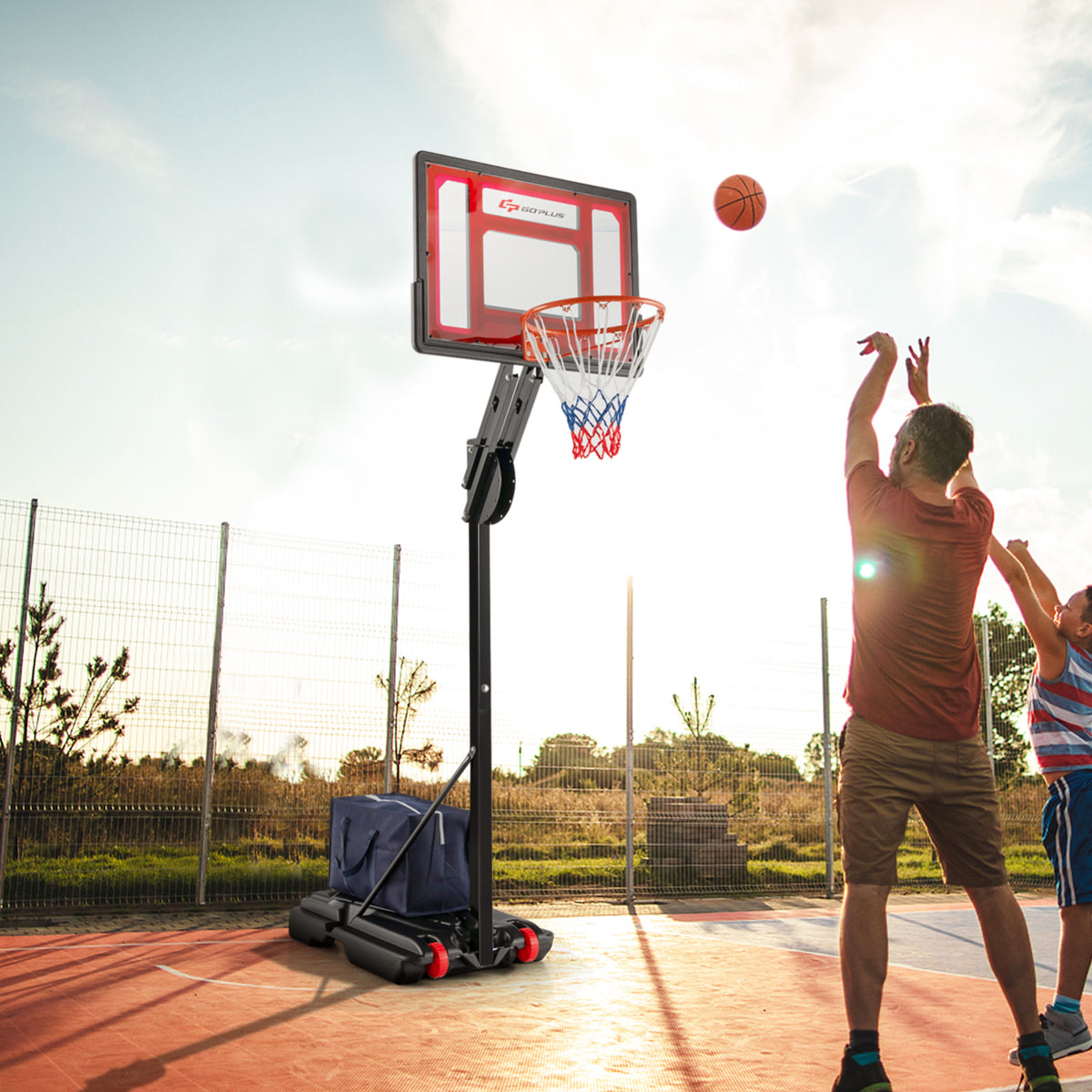 Two men play basketball with the adjustable hoop on an outdoor court at sunset