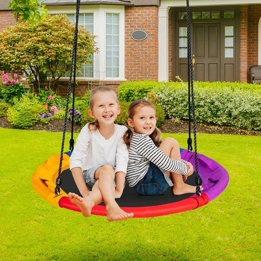Two smiling children sit on the colourful round saucer tree swing in a garden setting