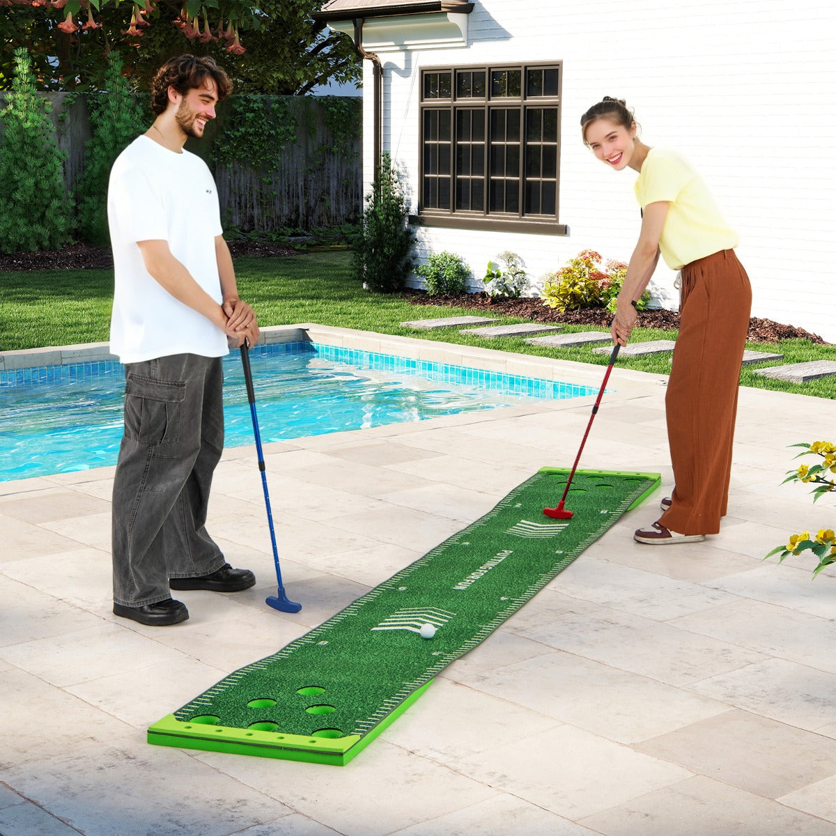 the putting green mat being used by a man and woman on a patio next to a swimming pool