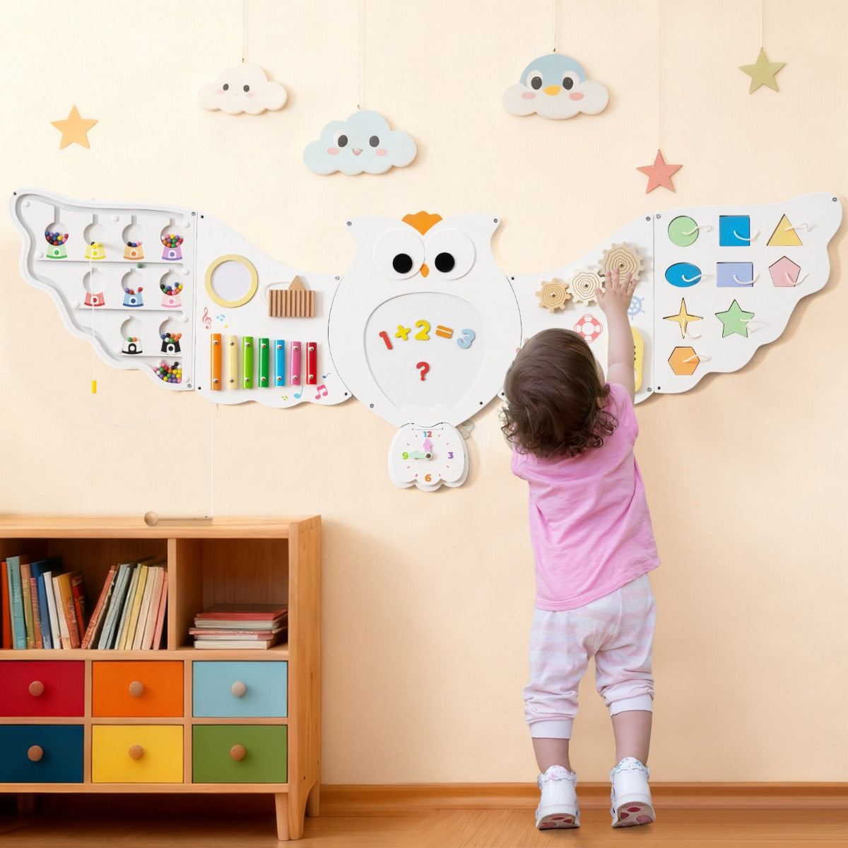 Child playing with the owl activity centre mounted on a wall above a bookshelf
