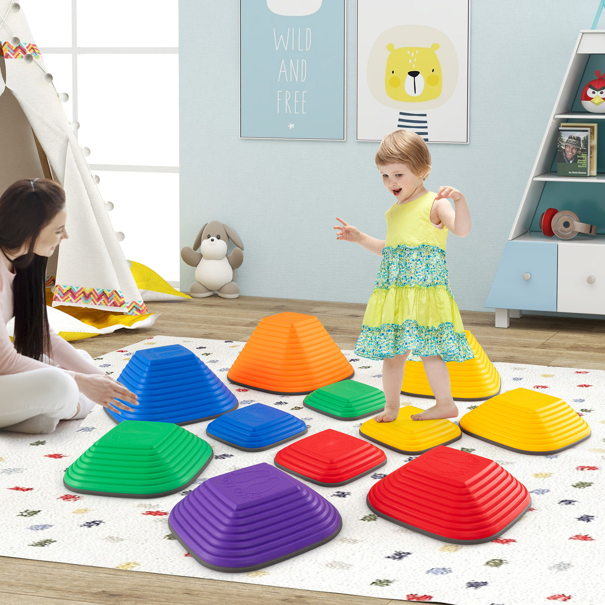 A young girl balances on a yellow stepping stone while a woman watches in a playroom