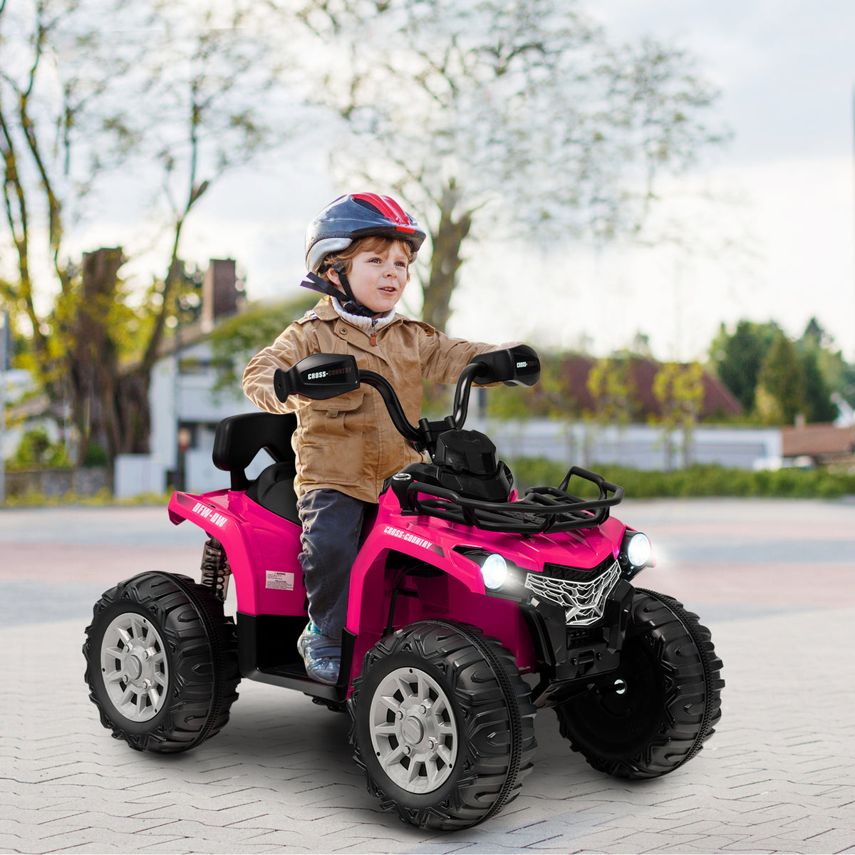 A young boy wearing a helmet riding the kids electric car on a paved driveway