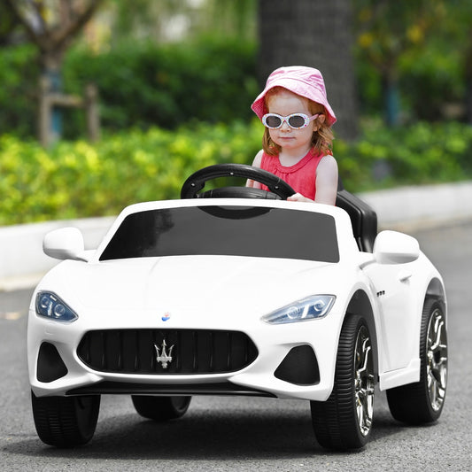 A young child wearing a pink hat happily driving the white kids electric car on a paved road