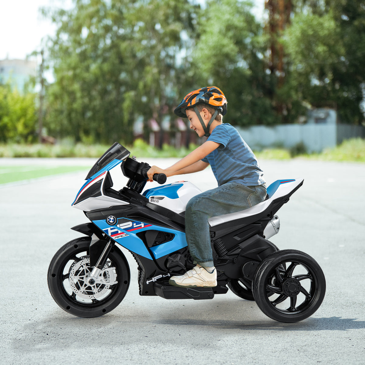 A young boy wearing a helmet rides a blue kids electric motorbike on a paved path