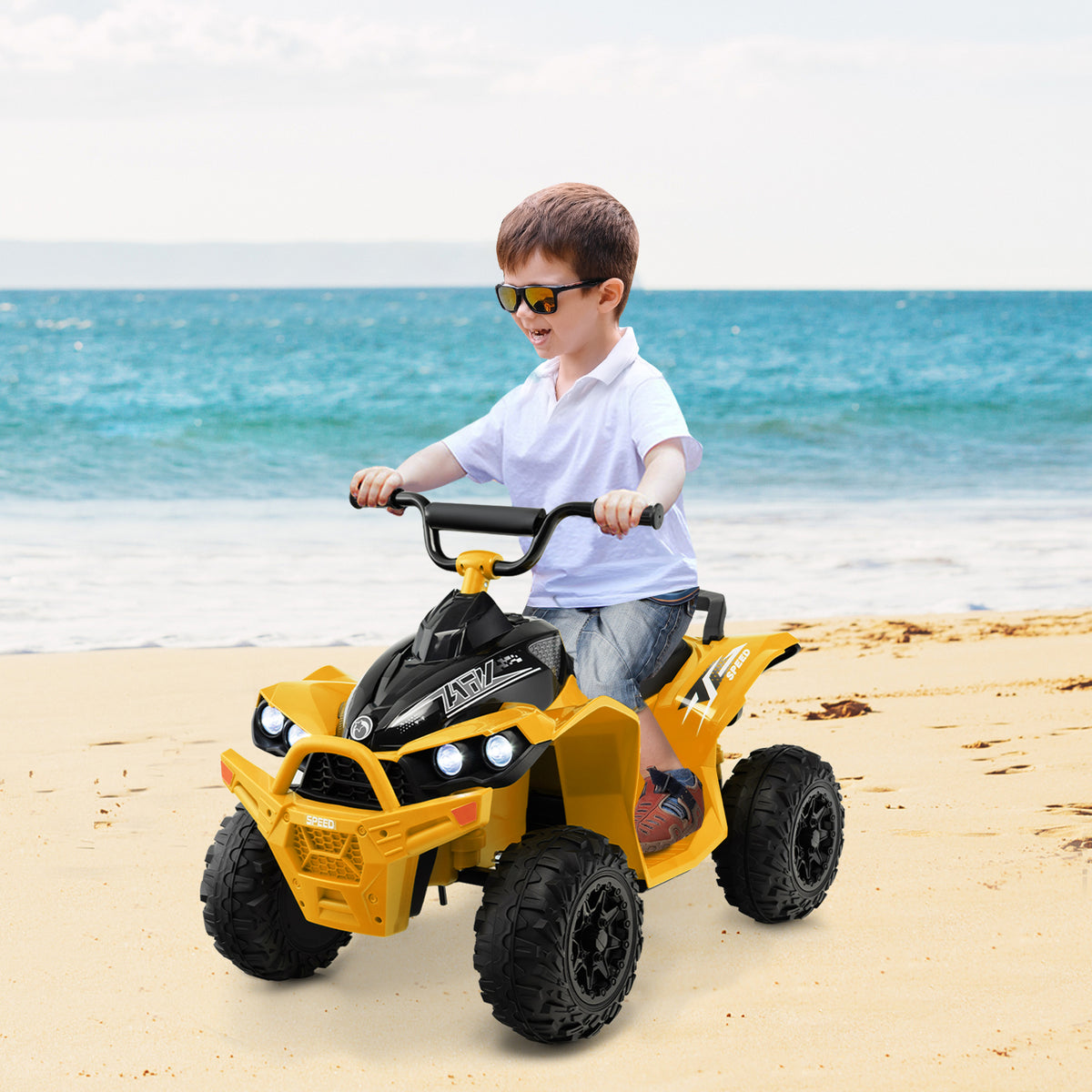 A young boy rides the yellow kids electric quad bike on a sandy beach