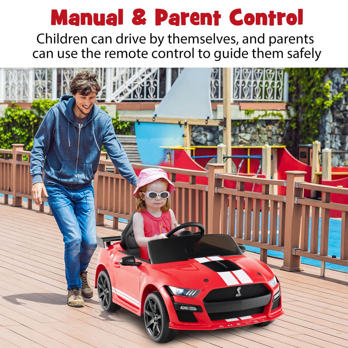The kids electric car being pushed by a man while a child sits inside on a wooden deck