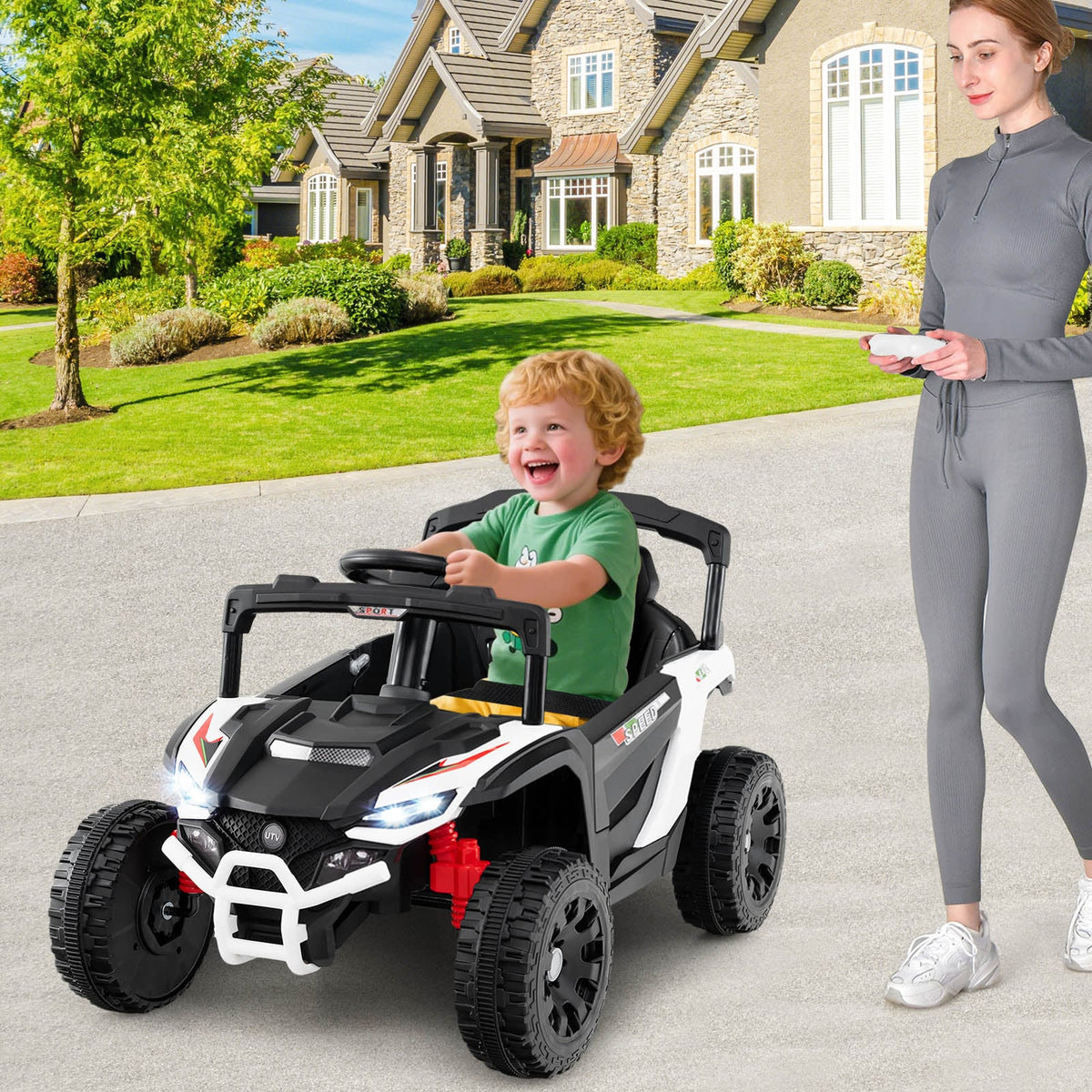 A woman stands next to a white kids electric UTV with a child sitting inside, on a paved driveway