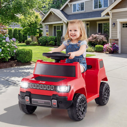 A young child driving the red kids electric car on a paved driveway outside a house