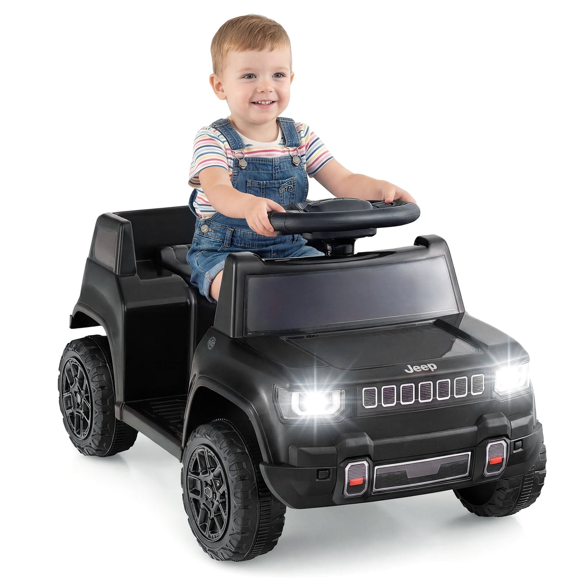 Smiling toddler in overalls steers the black electric jeep on grass