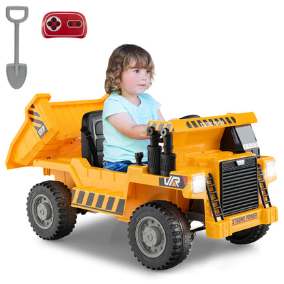 A young child sits in a yellow electric dump truck, with a remote control and shovel nearby