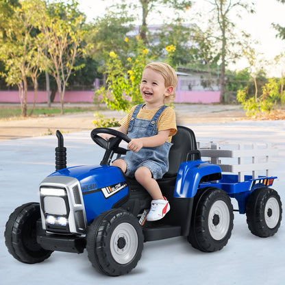 A happy young child drives the blue kids electric tractor with a trailer attached