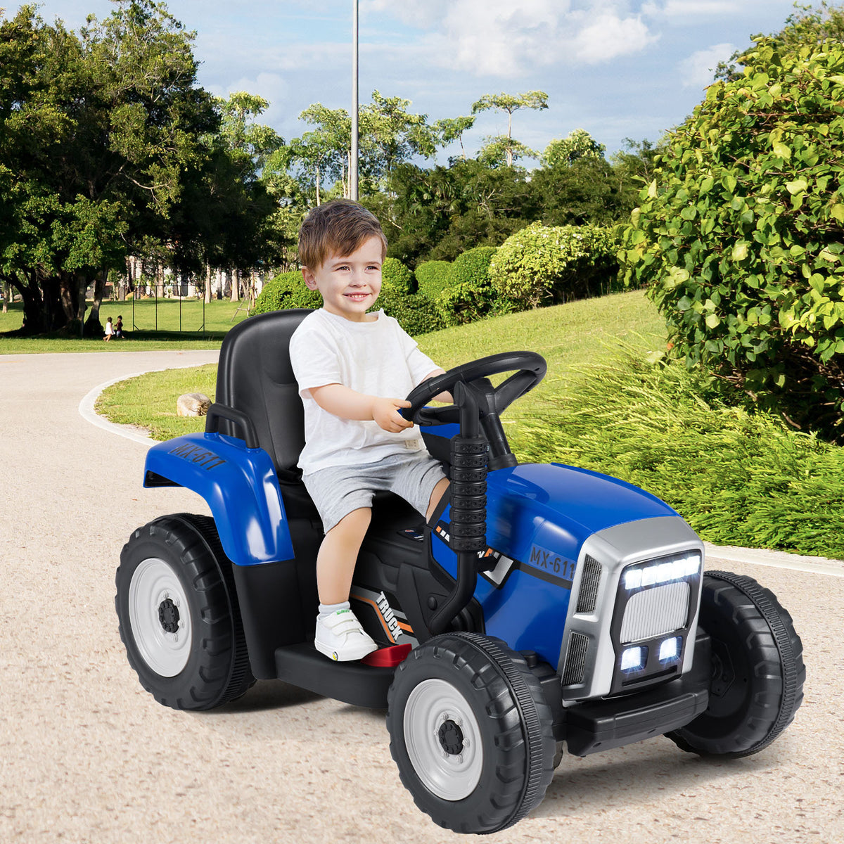 The blue kids electric tractor with trailer is shown from the side with a child at the wheel