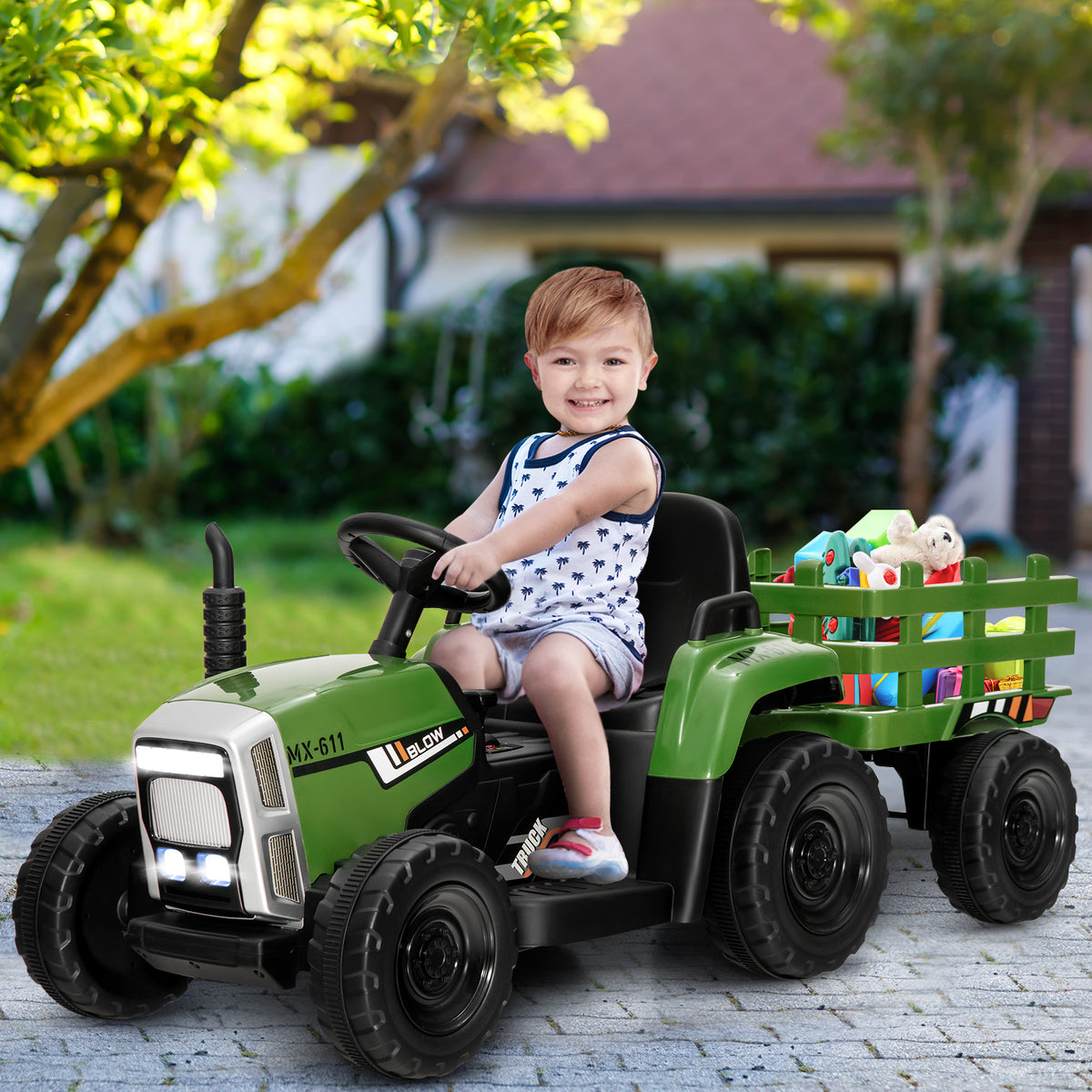 A young boy driving the kids electric tractor with a trailer full of toys on a patio