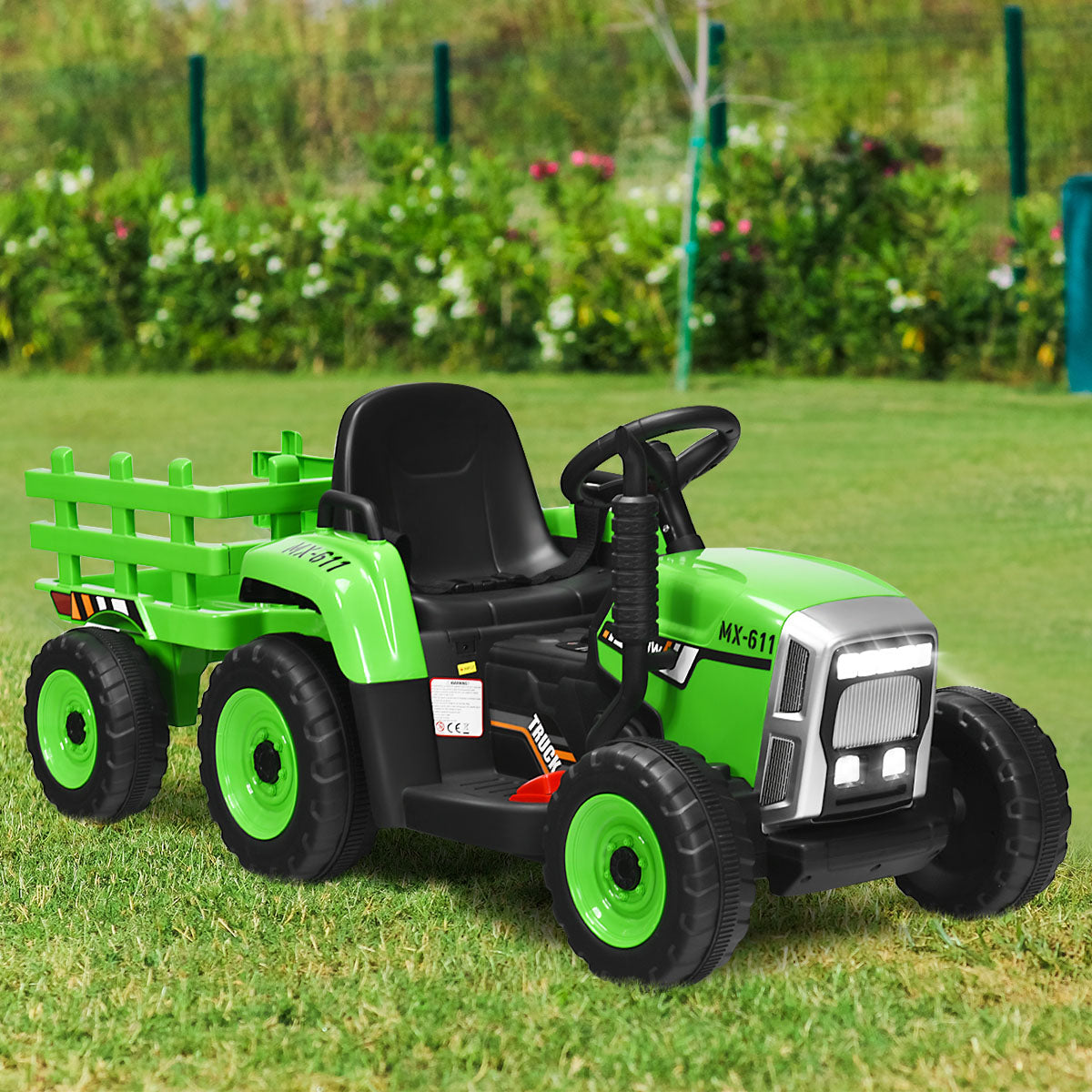 Green kids electric tractor with trailer parked on grass in a garden setting