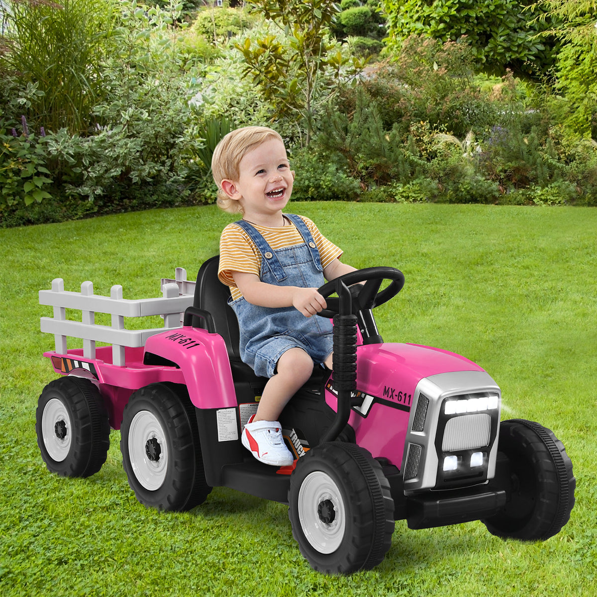 A happy toddler sitting in the pink kids electric tractor on a green garden lawn