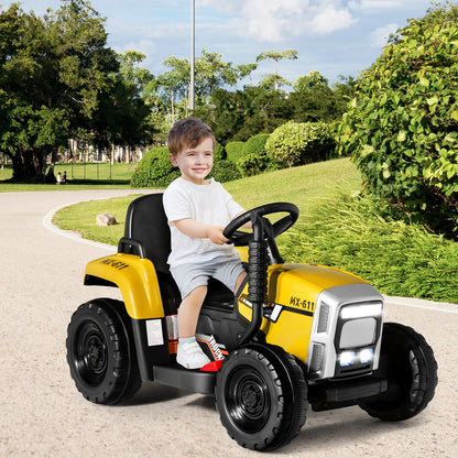 A young boy enjoys riding the yellow electric tractor with a trailer on a paved path in a park