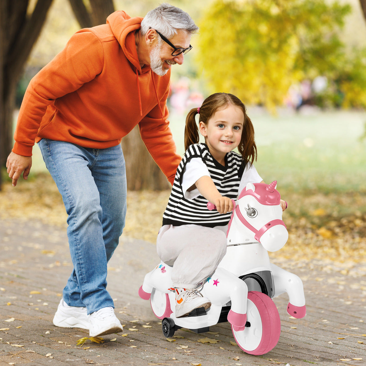 A little girl rides the pink unicorn electric toy while her grandfather pushes her