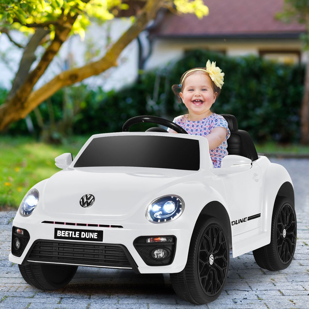 A happy child sits in the white electric ride on car, smiling at the camera