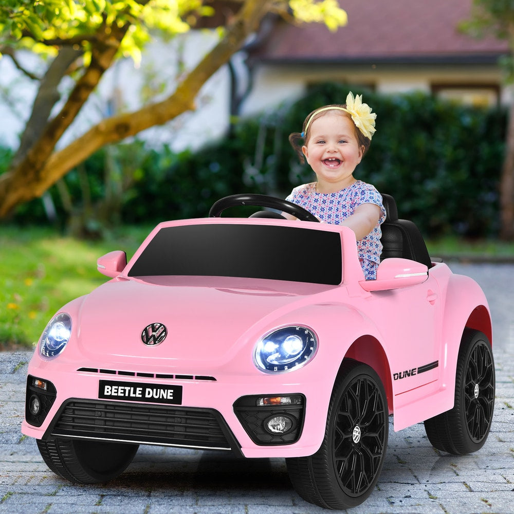 A happy child sits in the pink electric ride on car on a paved path