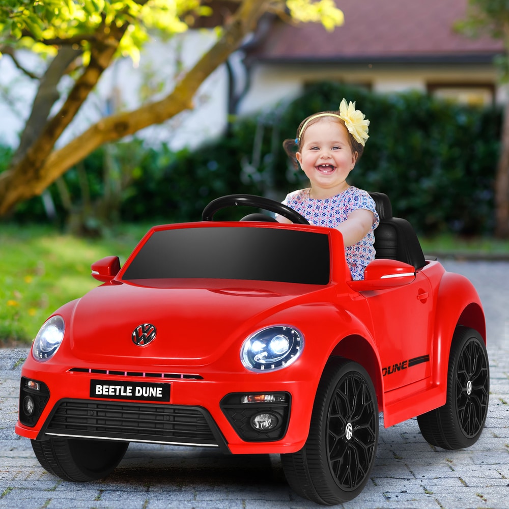 Happy toddler girl driving the red kids electric ride on car in a garden