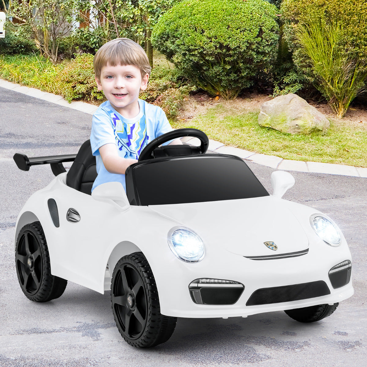 A young boy happily rides the white kids electric car on a paved path outdoors