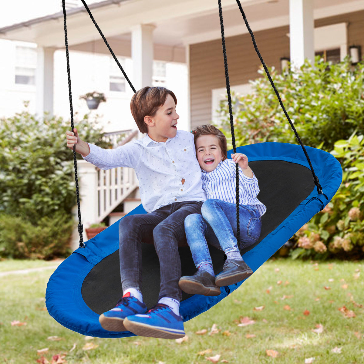 Two boys laughing while sitting on the blue oval swing in a backyard