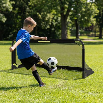 A boy kicks a soccer ball towards the goal in a grassy outdoor area
