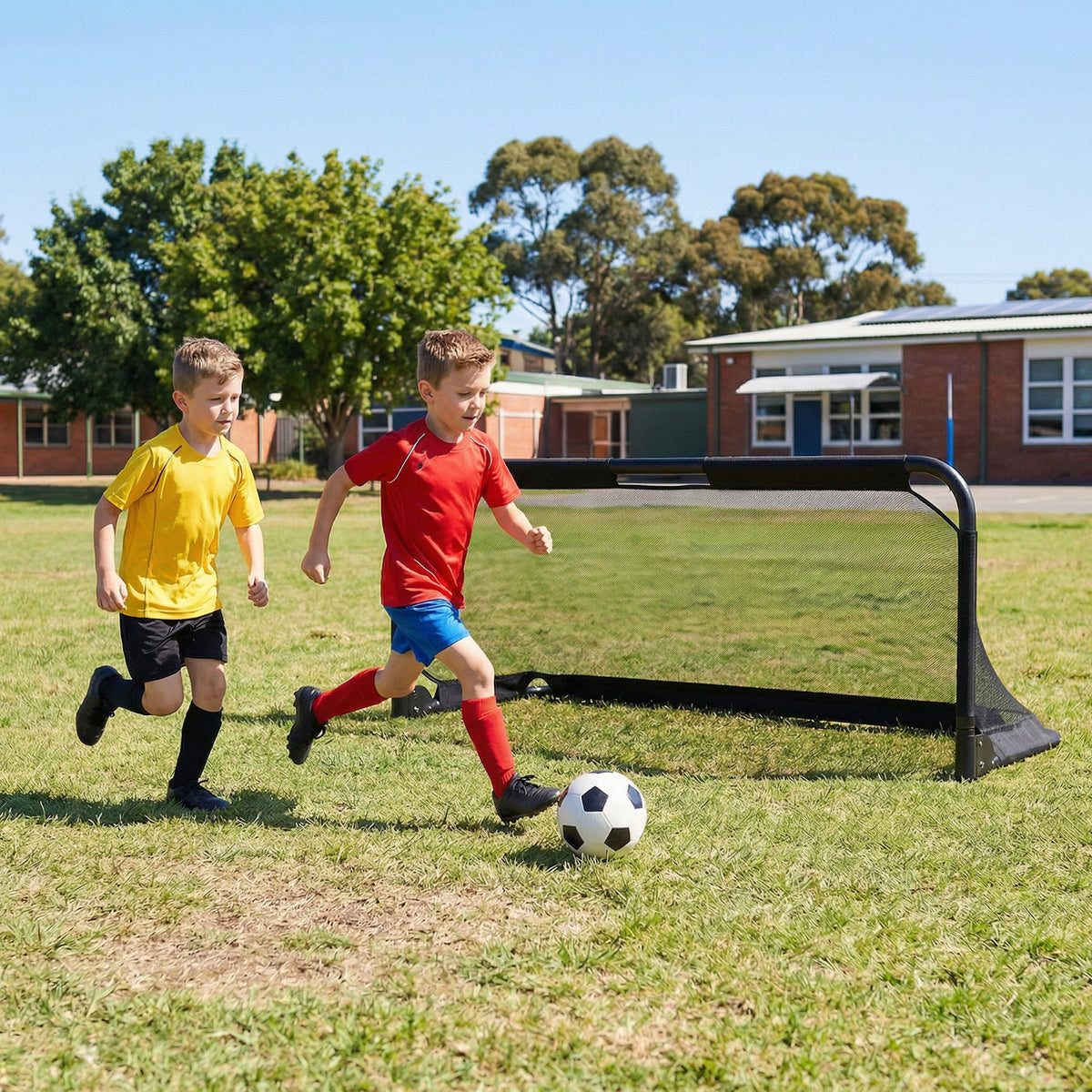 Two boys play soccer in front of a school building with the goal set up