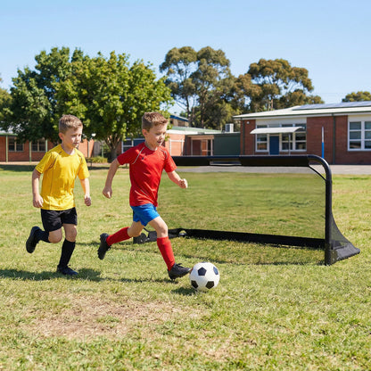Two boys play soccer in front of a school building with the goal set up