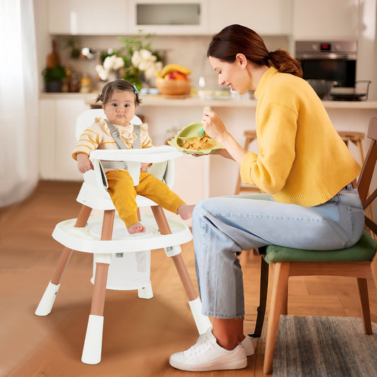 A baby sits in the white convertible high chair while a woman feeds her at a table