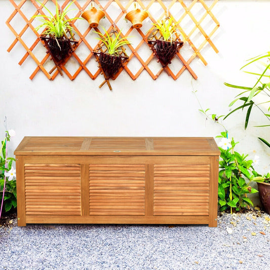 180L Acacia Wood Deck Box, the outdoor storage box placed on a gravel path in front of a wall with hanging plants