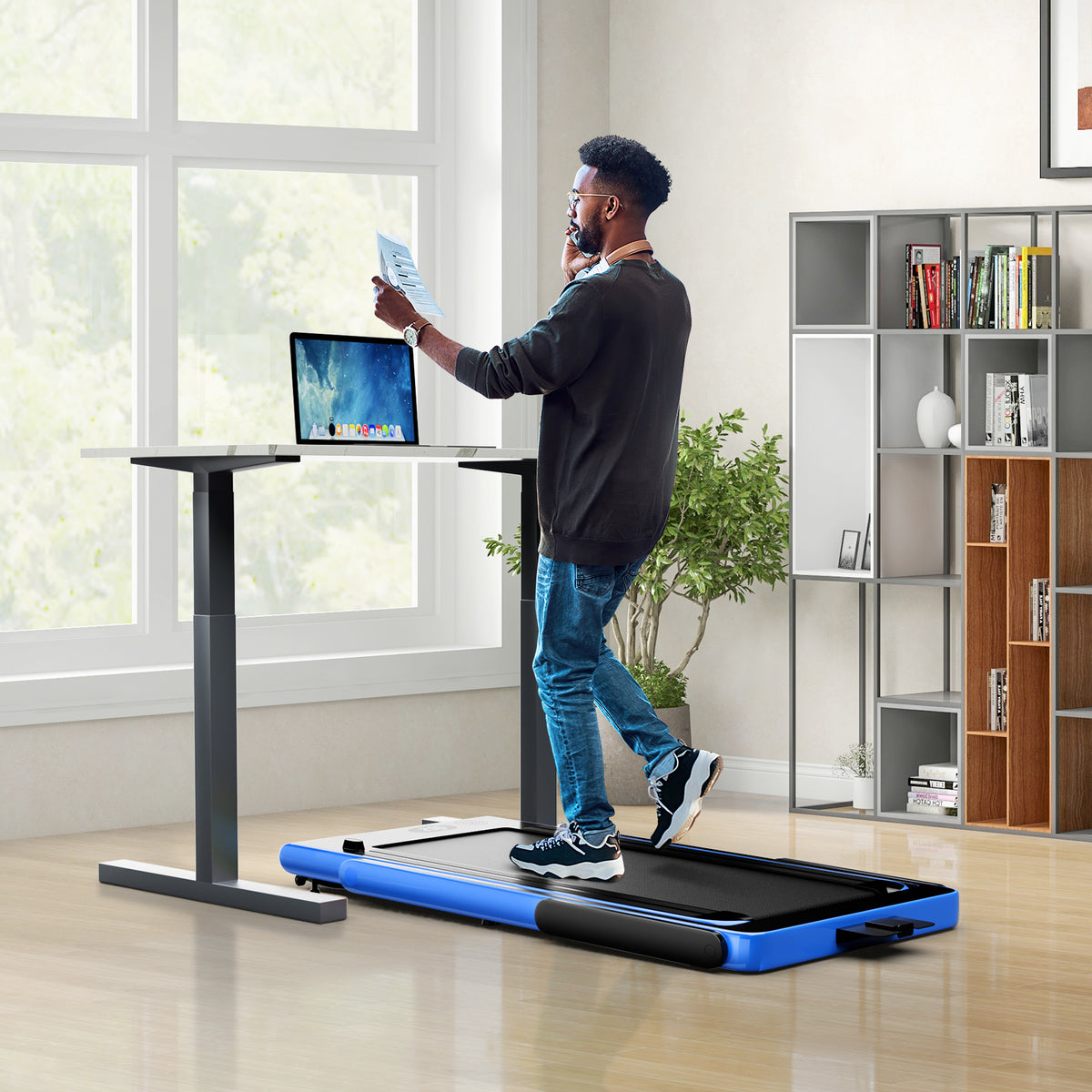 The treadmill under a standing desk, a man using it while working