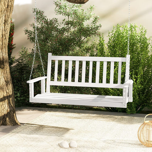 White wooden porch swing hanging from a tree branch in a garden setting