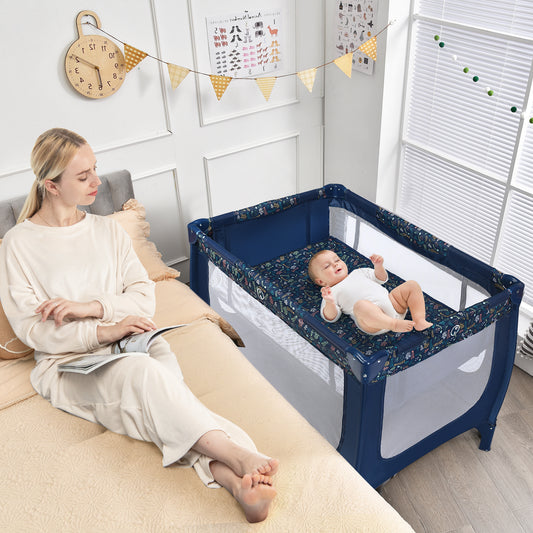 Woman reading on a bed next to the blue baby playpen with a baby inside