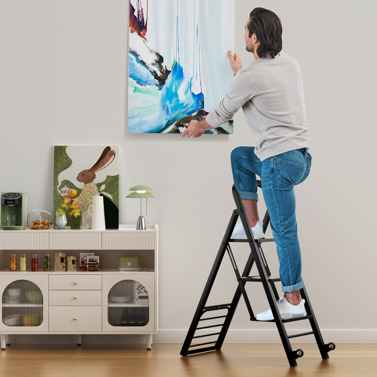 The foldable ladder being used to hang a picture