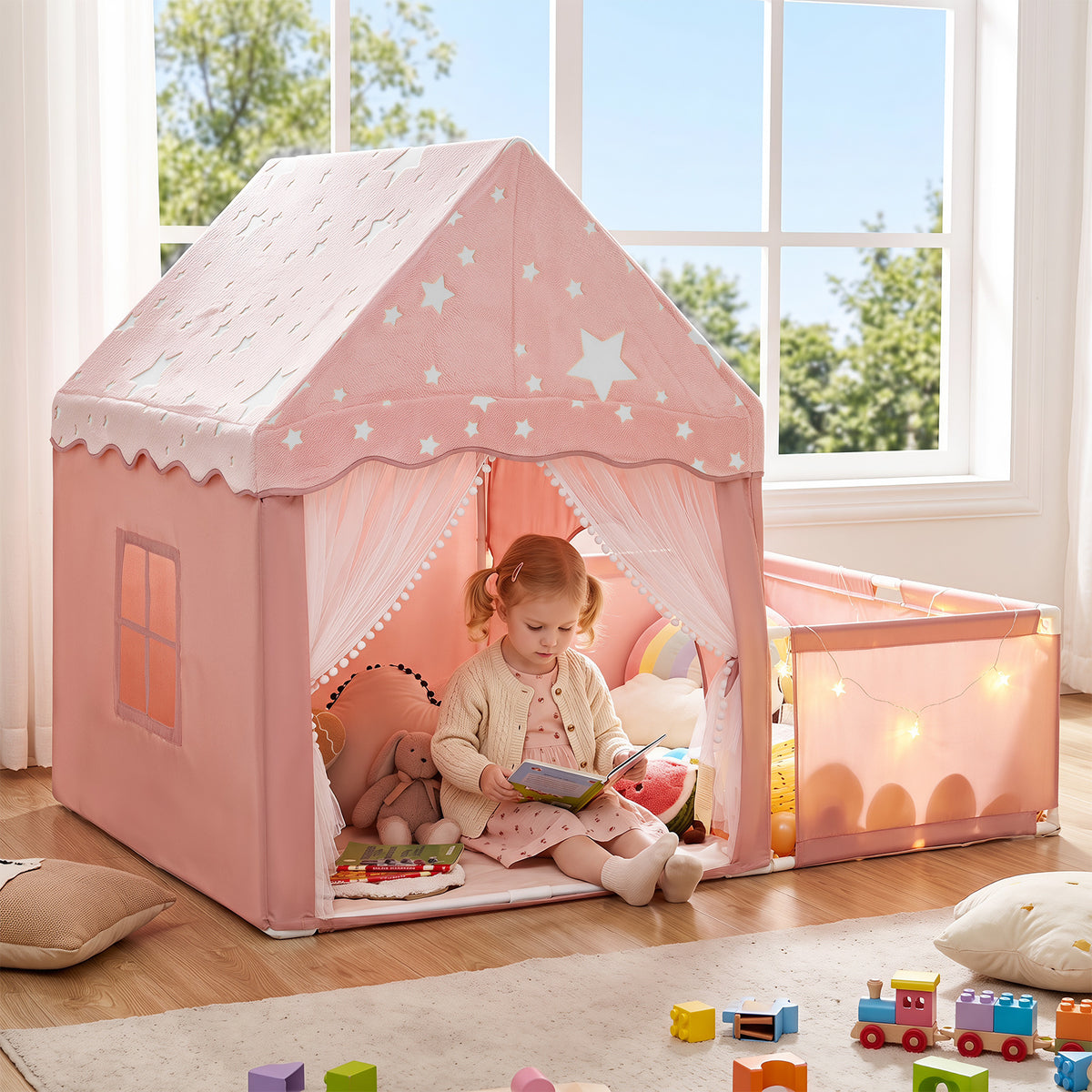 A young girl reads a book inside the pink kids play tent with the playpen attached