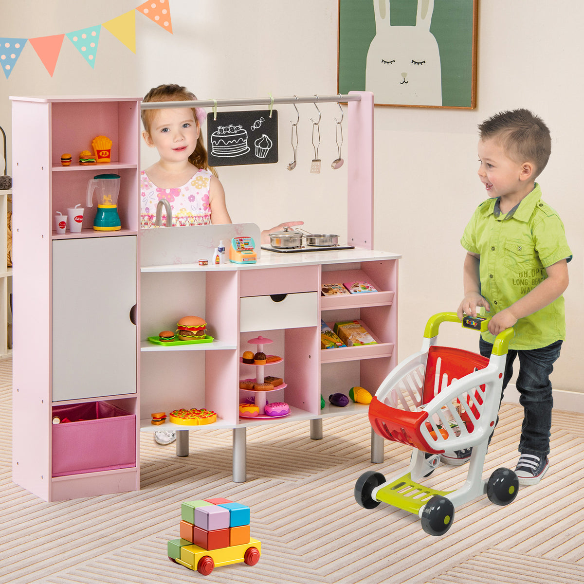 Children playing with the pink play kitchen and market set, one child at the counter and another with a shopping trolley