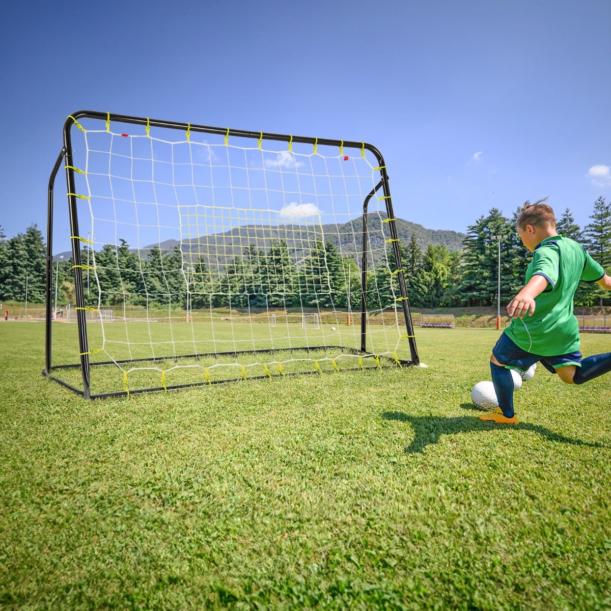 Soccer goal with a rebounder net in a grassy field with a boy kicking a ball