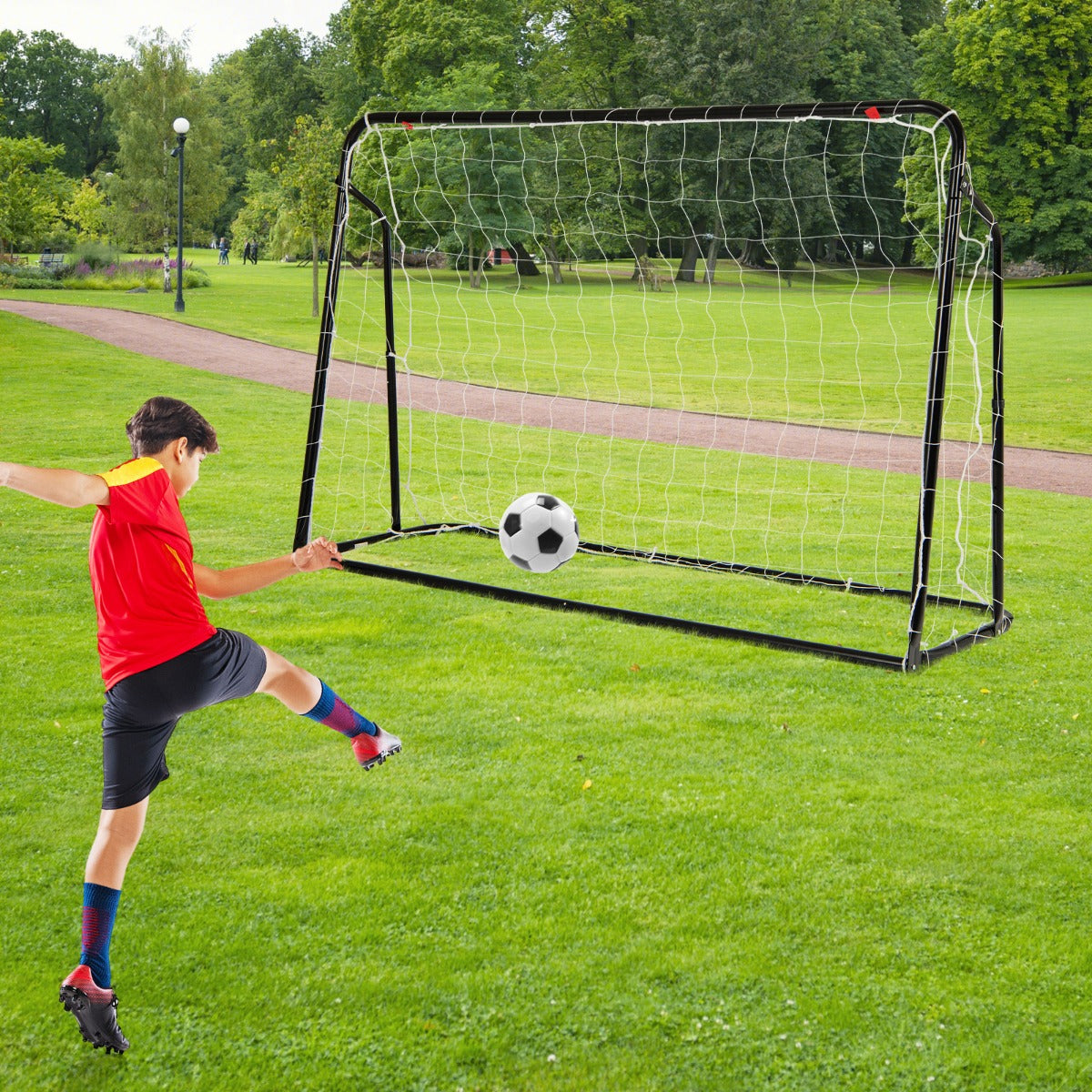 Young boy in a red shirt kicking a soccer ball towards the soccer goal in a park