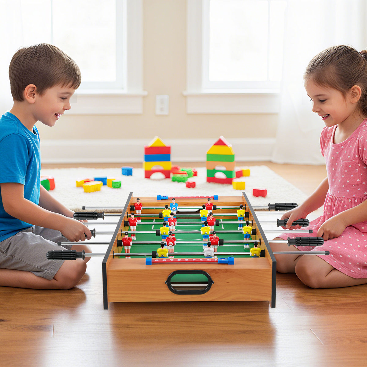 A boy and a girl sitting on the floor playing a foosball match on the compact game board