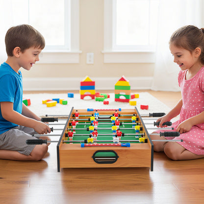 A boy and a girl sitting on the floor playing a foosball match on the compact game board
