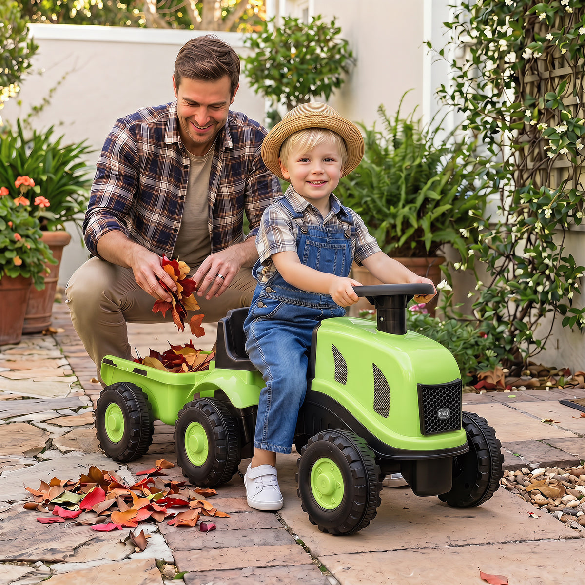 A father and child play with the green ride on tractor with trailer outdoors