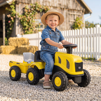 The yellow ride on toy being used by a smiling child in a gravel driveway near a wooden barn