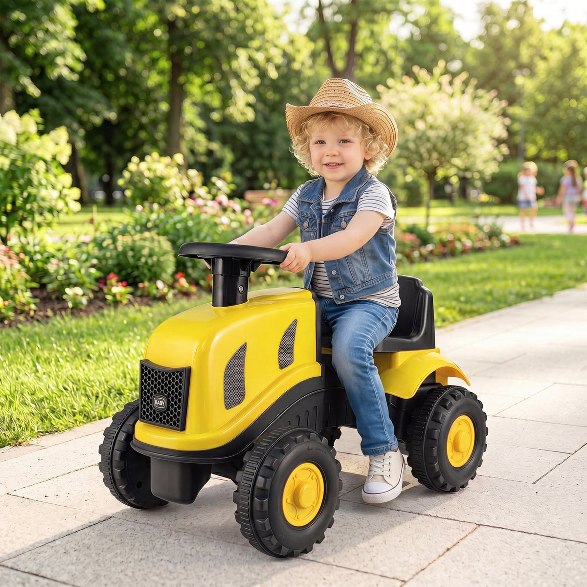 The yellow ride on toy being driven by a child on a paved path in a park with green trees