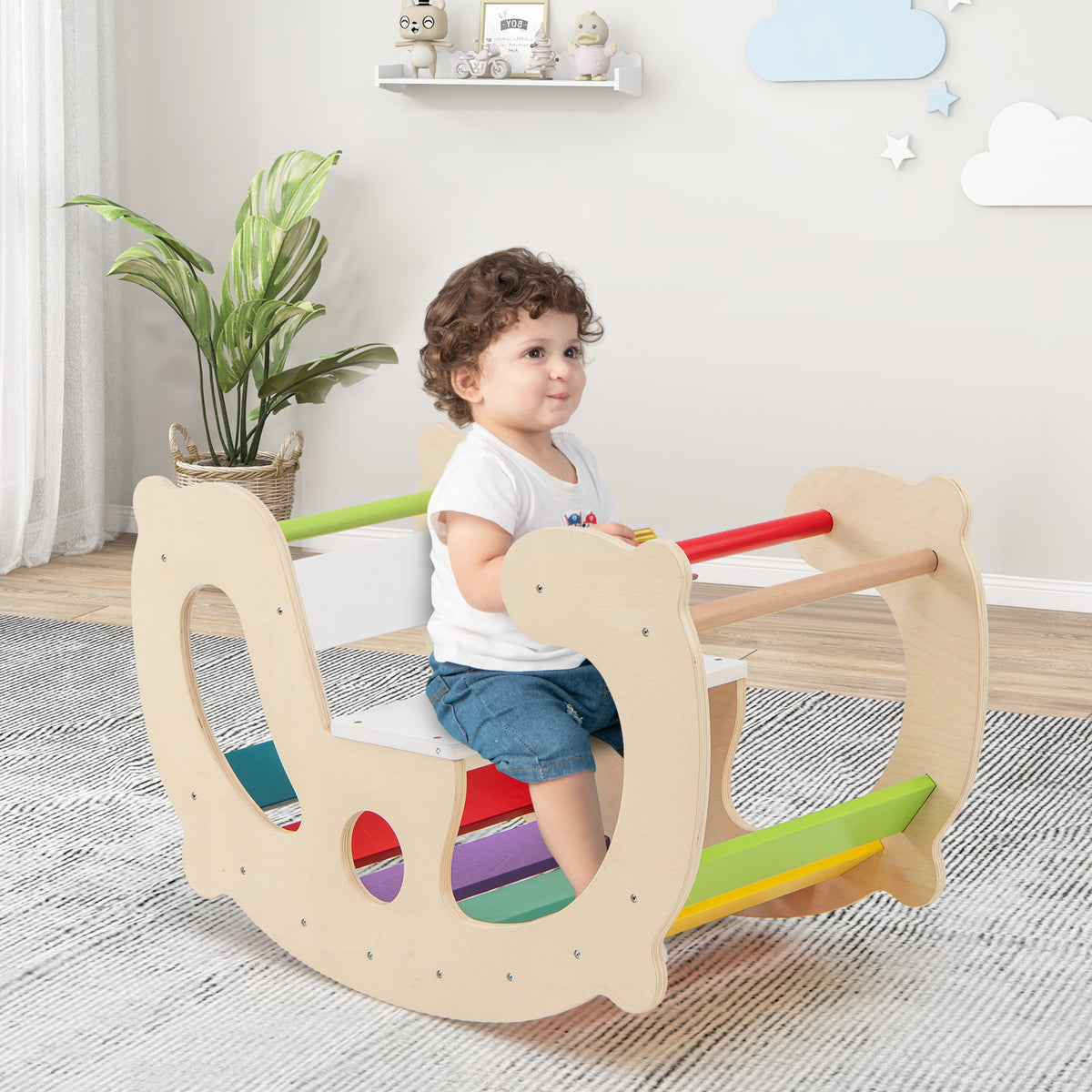 A toddler sits on the natural wood rocking horse arch with colourful rainbow steps