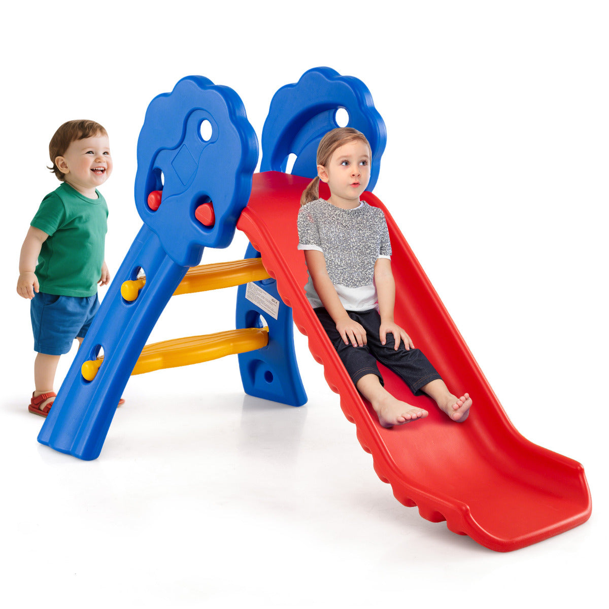 Two toddlers playing on the red and blue slide indoors